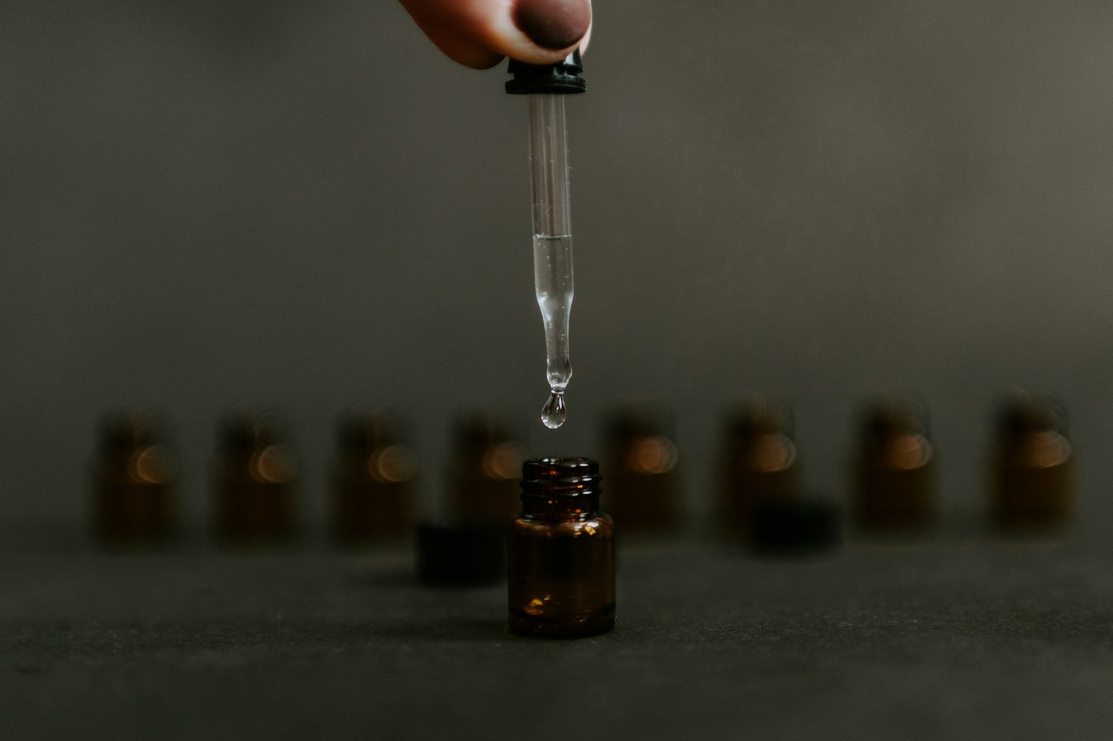 A glass dropper releasing a drop of clear serum into an amber bottle