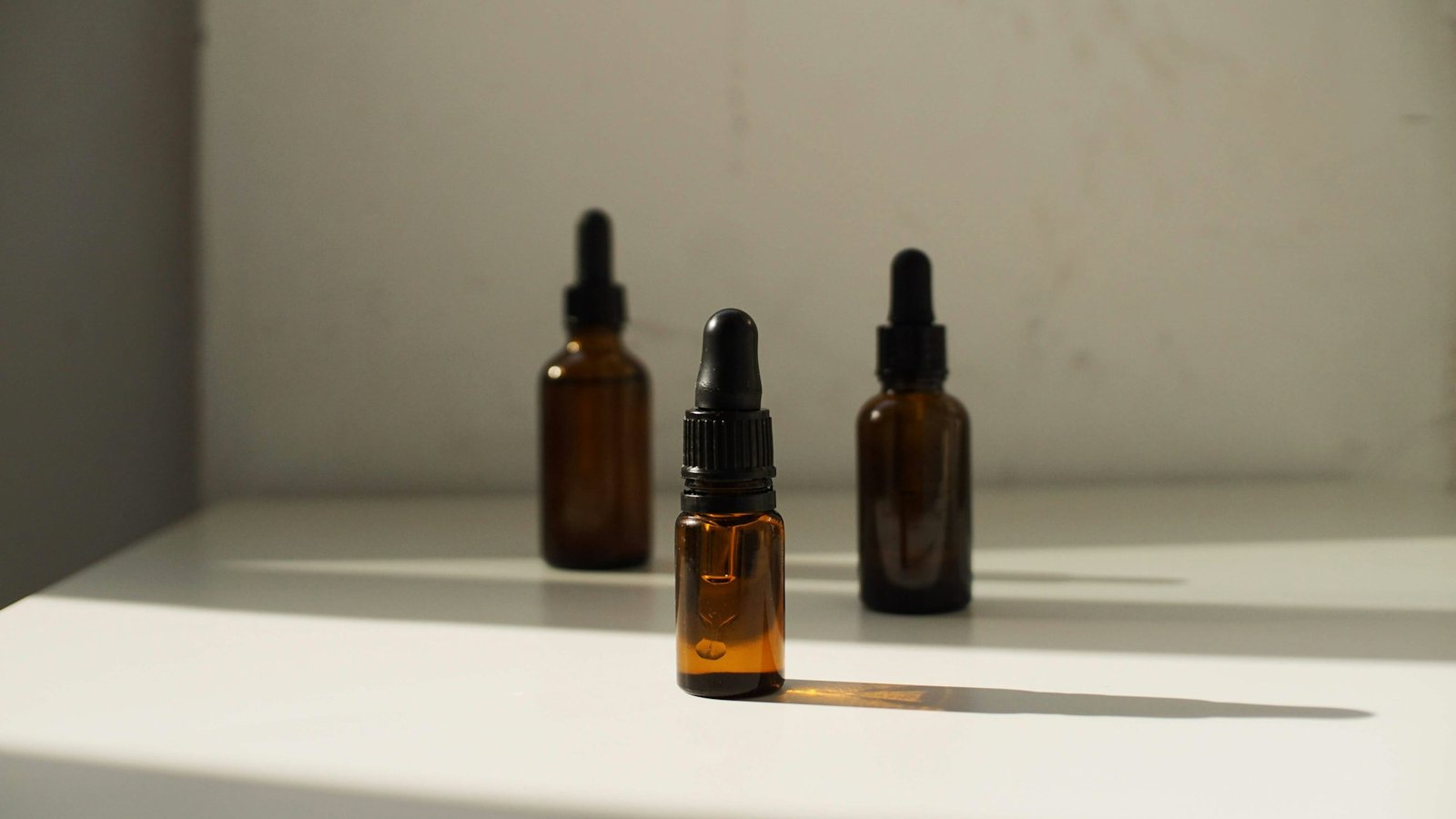 Three amber glass dropper bottles of skincare serums on a sunlit shelf