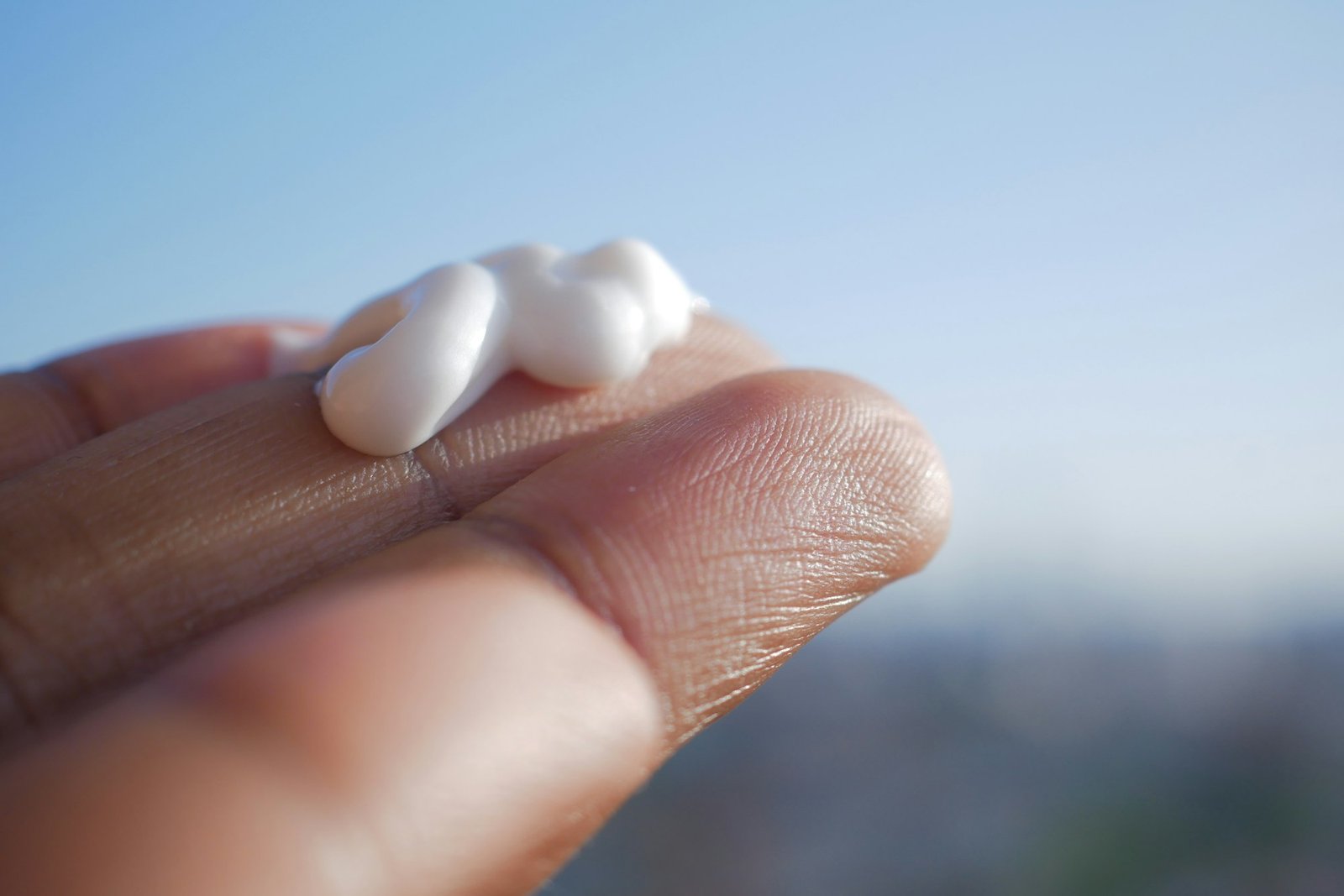 A dollop of white sunscreen on fingertips against a blue sky
