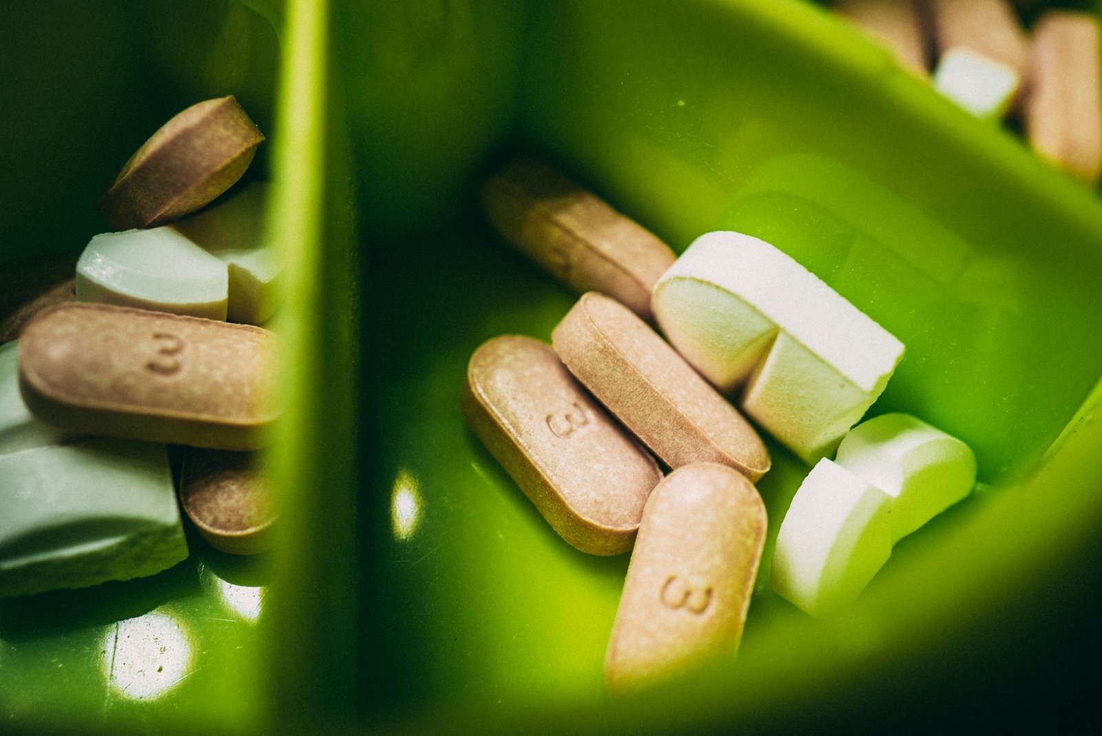 Vitamin tablets and capsules sorted in a green weekly pill organizer