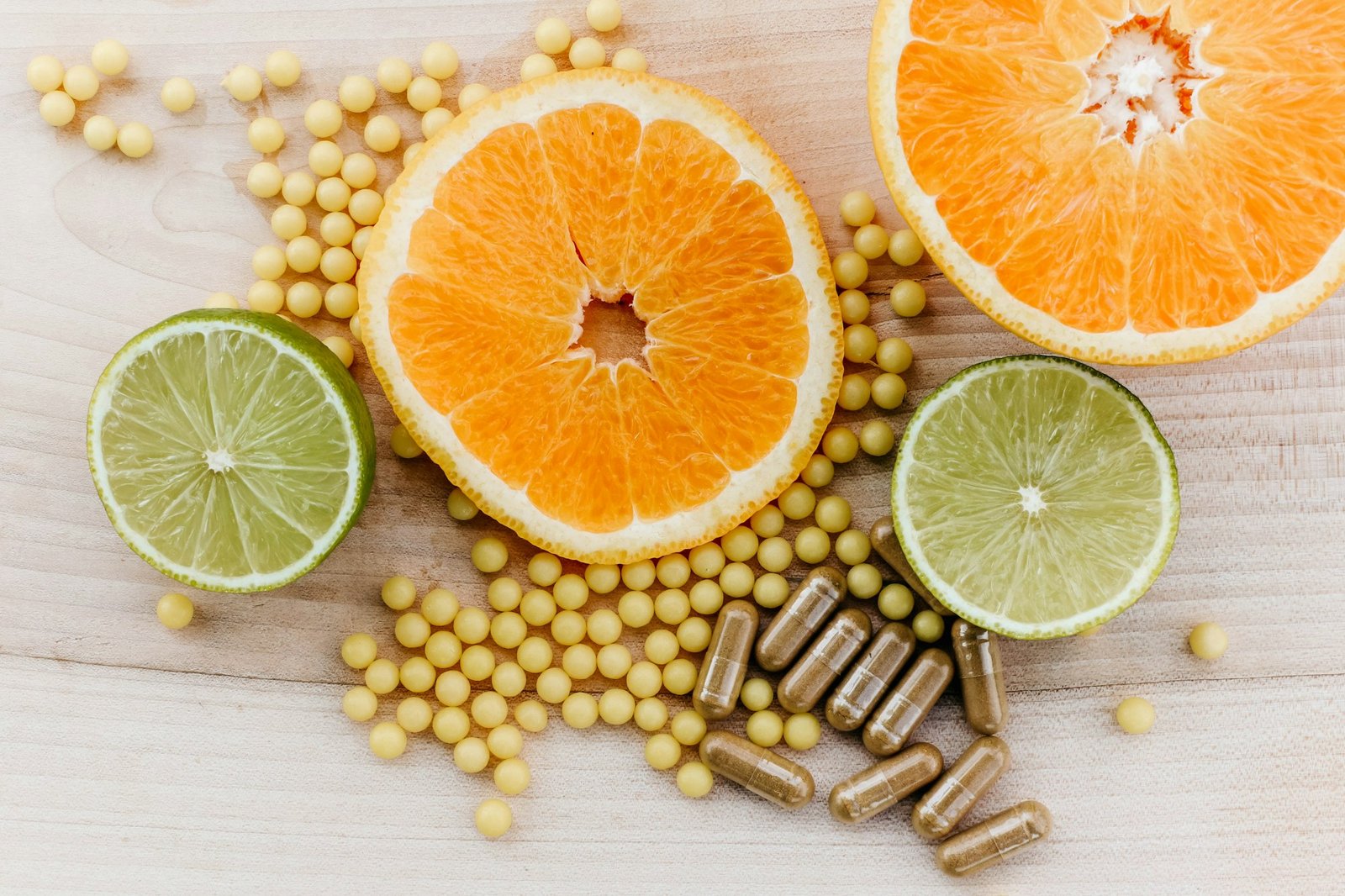 Sliced oranges and limes surrounded by supplement beads and capsules on a wooden table